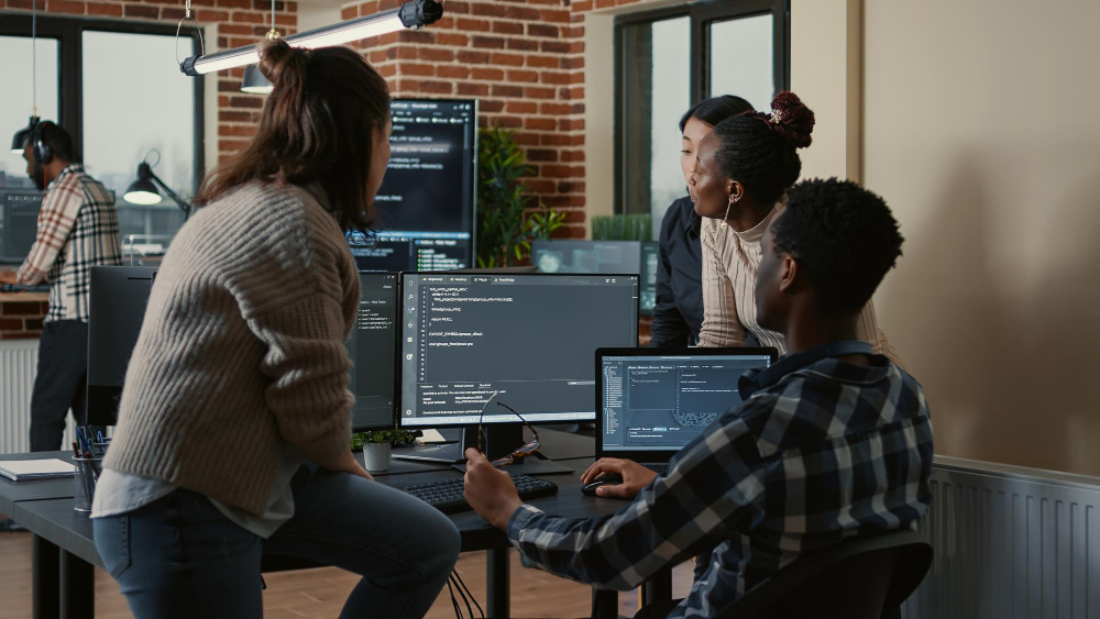 Software developers crowded around a computer with multiple screens looking at coding to represent Azure DevOps